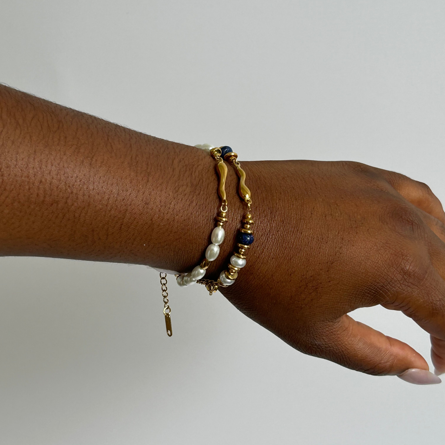 Hand wearing multiple bracelets on a plain background