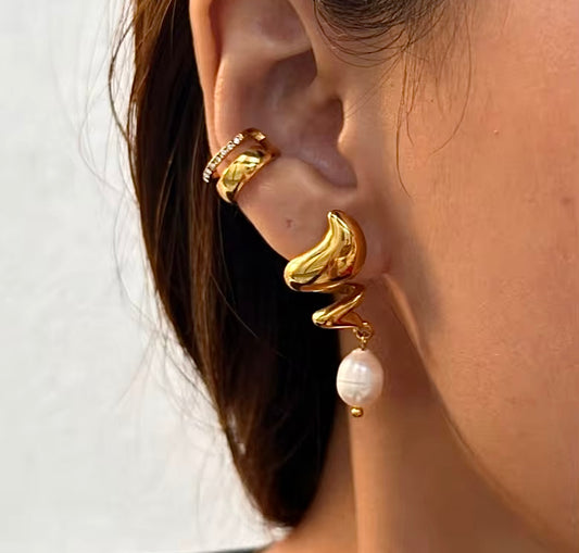Gold earring with a pearl drop worn by a person against a white background