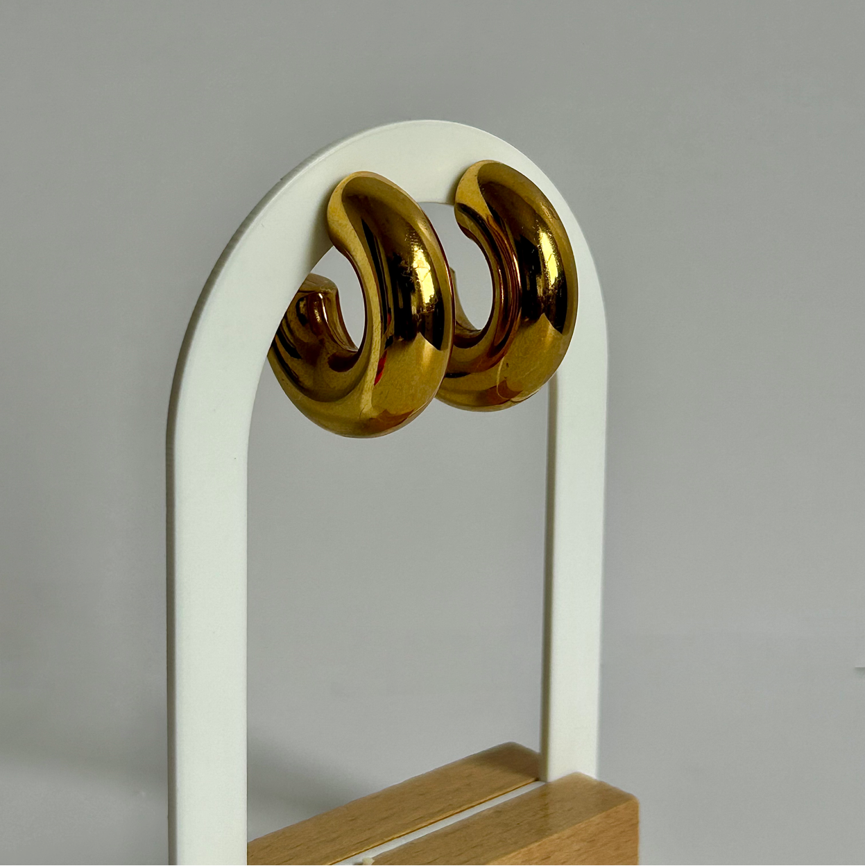 Gold earrings on a white stand with a gray background
