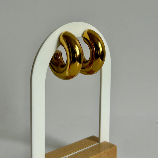 Gold earrings on a white stand with a gray background