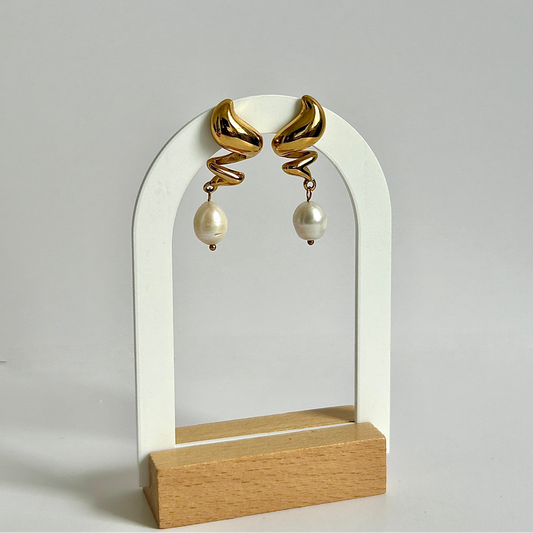 Gold spiral earrings with pearl drops on a white arch stand against a light gray background